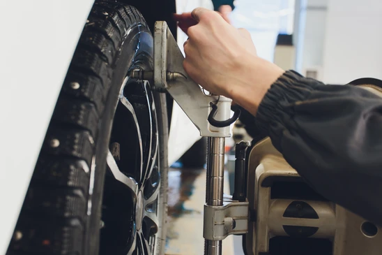 Technicien en combinaison professionnelle effectuant un calibrage ADAS ou une géométrie des roues, utilisant un équipement de mesure de précision (portique de géométrie ou scanner ADAS) dans un atelier automobile moderne, avec le véhicule positionné sur une plate-forme de diagnostic, dans un environnement professionnel clair et bien éclairé.